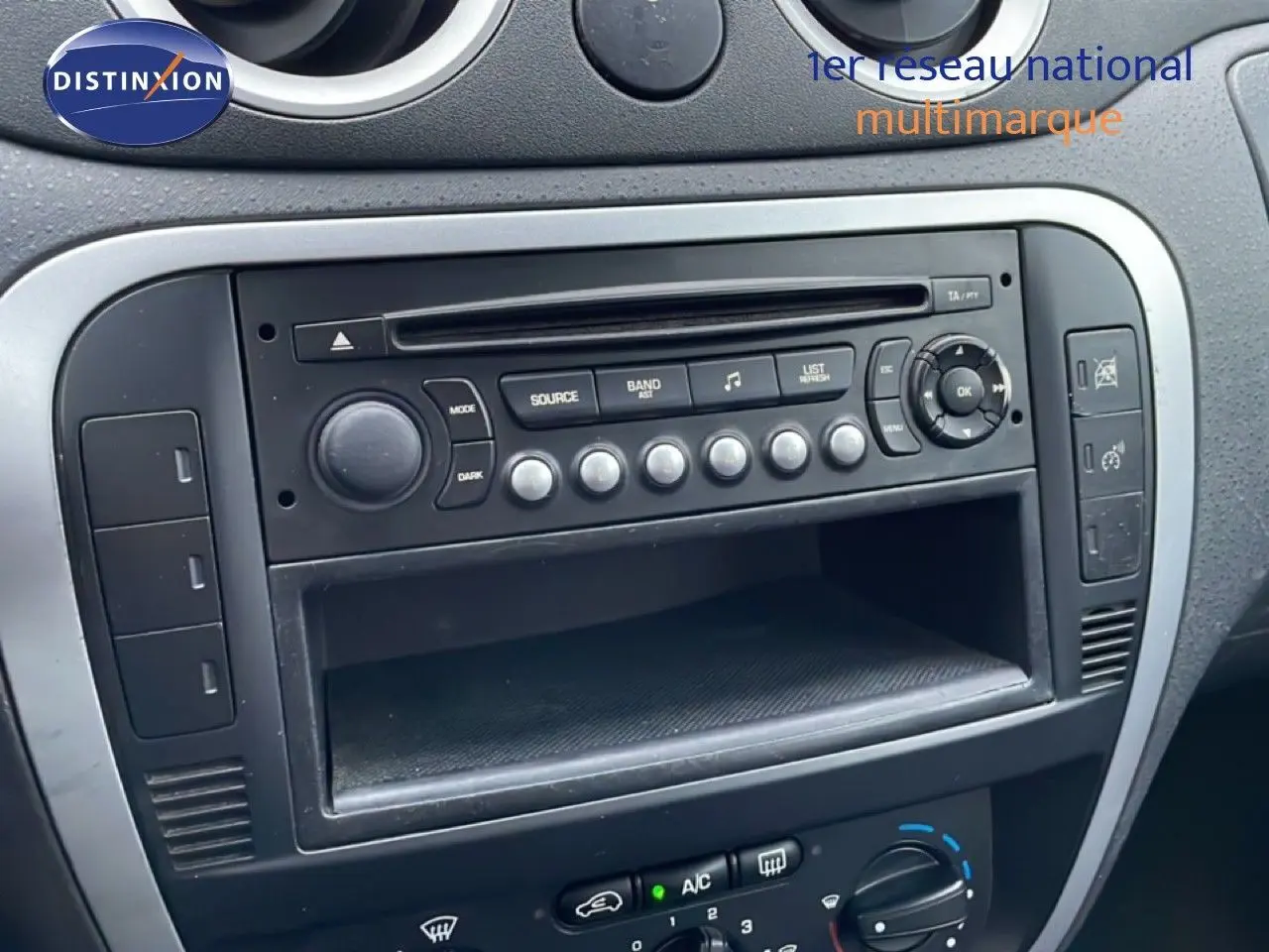 Vue rapprochée de la console centrale noire d’une Citroën C3 Pluriel 1.4 HDI 70CH avec autoradio et commandes de climatisation.