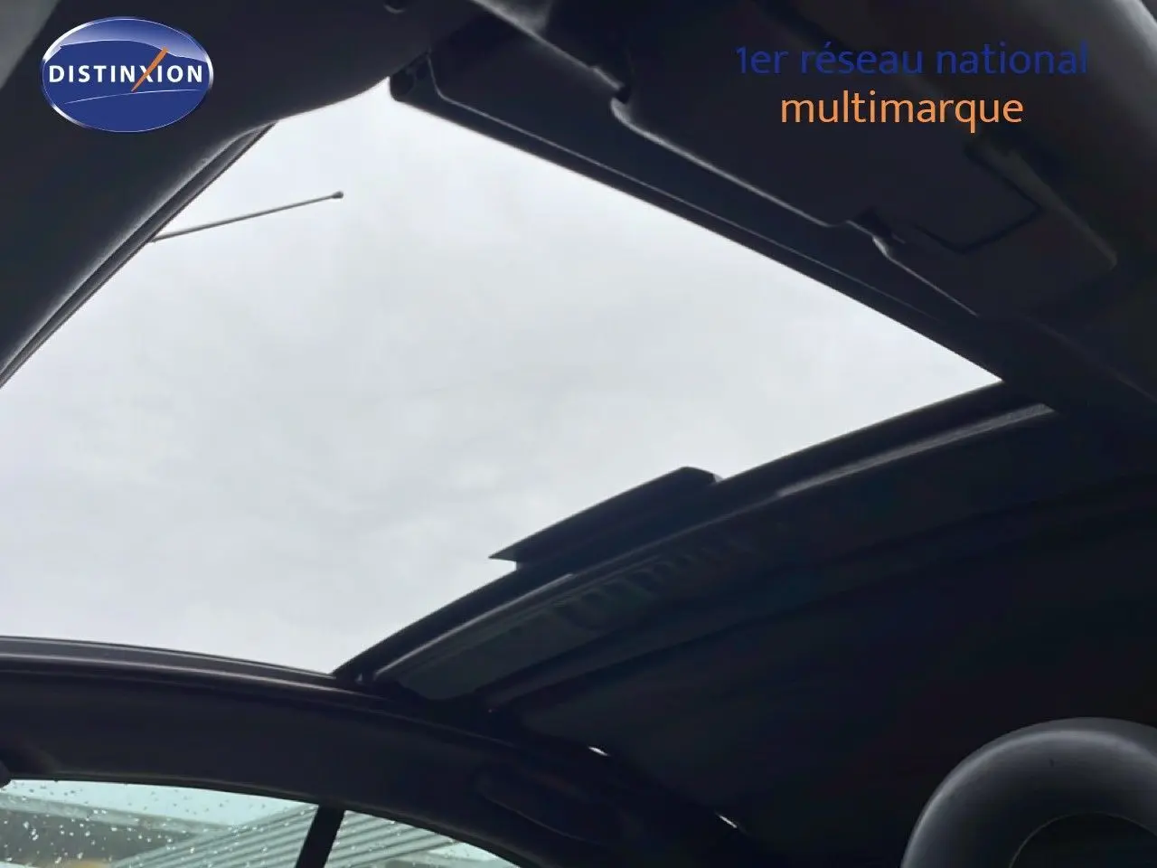 Toit ouvrant panoramique ouvert sur une Citroën C3 Pluriel ivoire, vue intérieure vers le ciel gris.