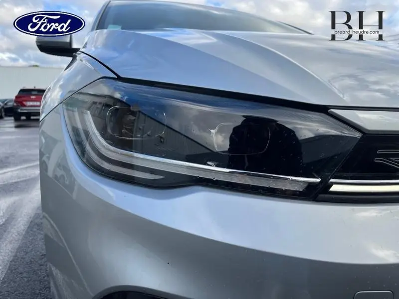 Gros plan sur le phare avant gauche d'une Volkswagen Polo Reflet d'Argent métallisé, avec calandre partielle visible.