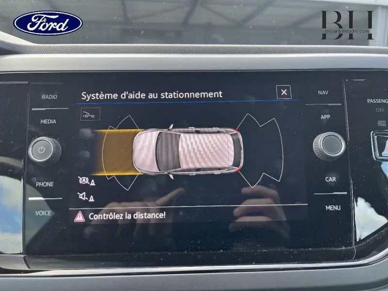 Écran tactile du système d'aide au stationnement montrant une voiture vue de dessus avec zone de détection en jaune.
