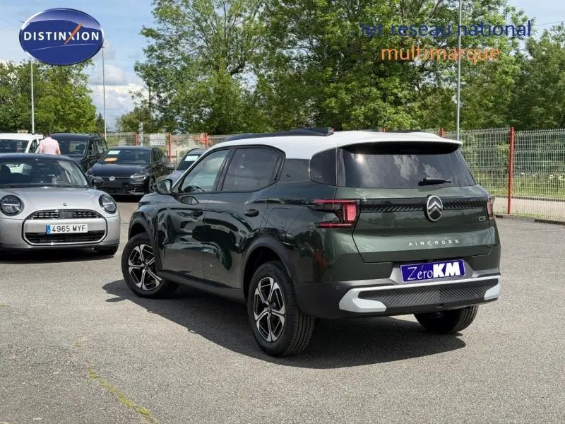 Vue 3/4 arrière droite d'un Citroën C3 Aircross vert Montana avec toit blanc et jantes alu, en extérieur sur parking.