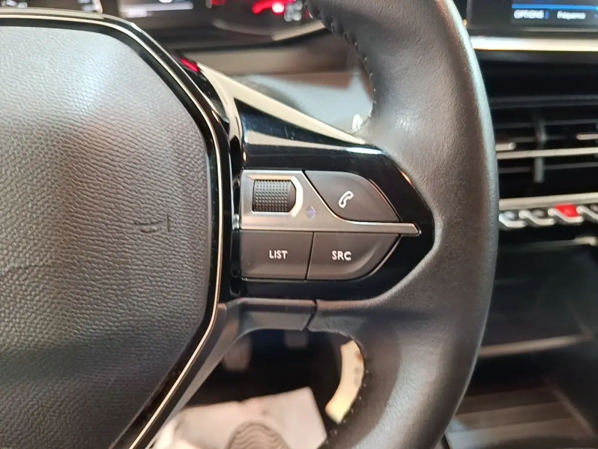Gros plan sur le volant cuir multifonctions de la Peugeot 208 gris clair, avec commandes audio et téléphone intégrées.
