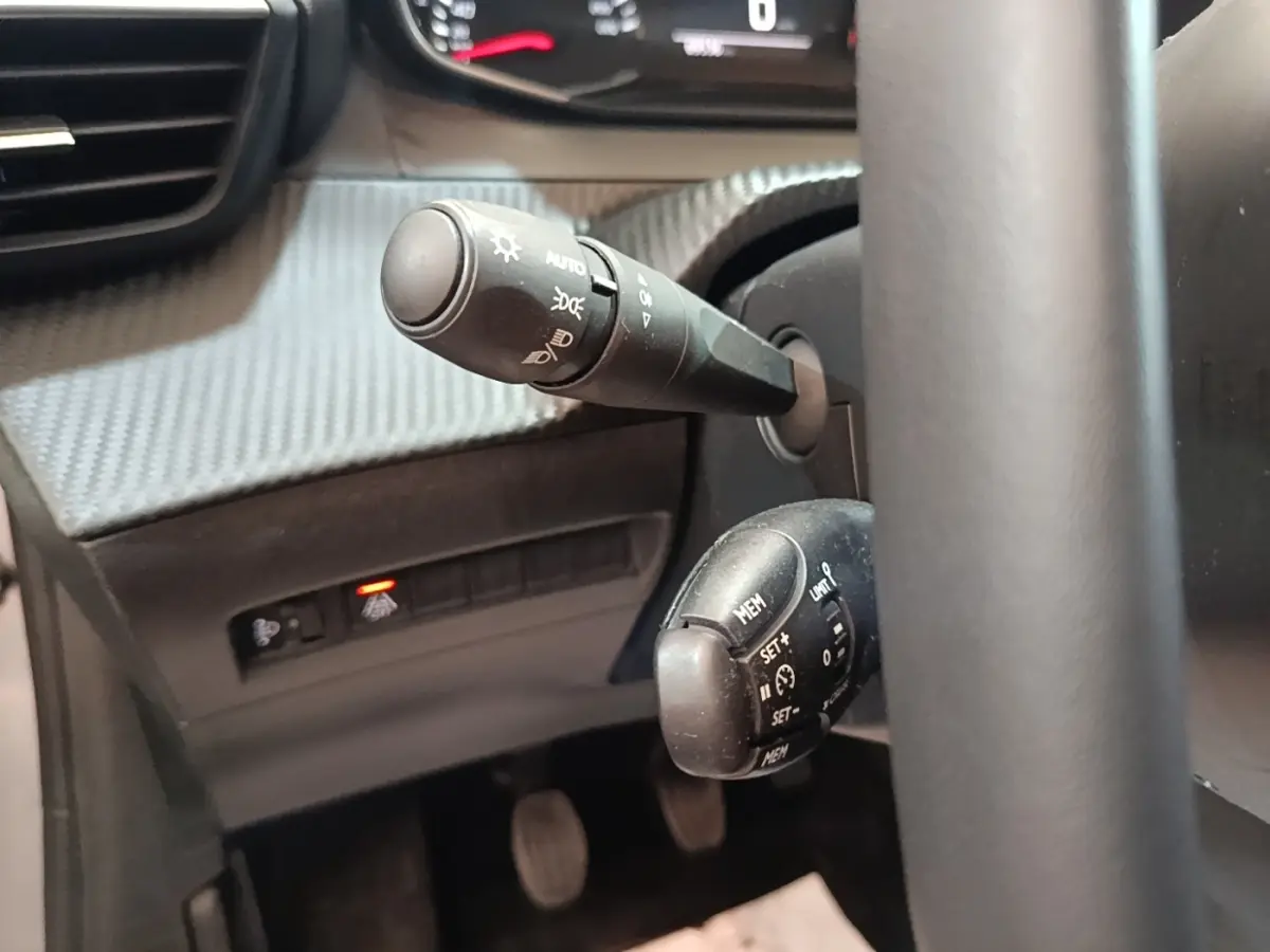 Gros plan sur les commandes au volant cuir de la Peugeot 208 gris clair, avec réglage régulateur de vitesse et éclairage automatique.