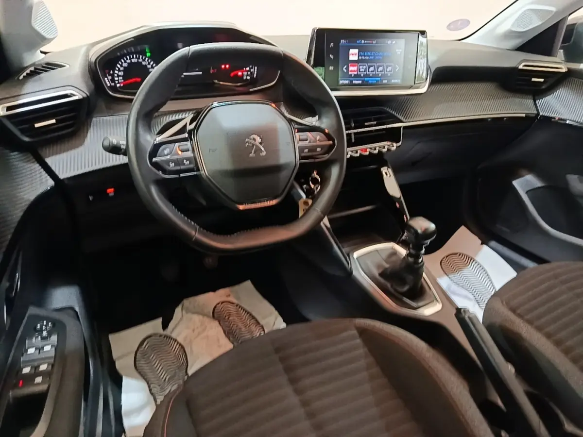 Vue intérieure avant de la Peugeot 208 gris clair, volant cuir multifonctions et écran tactile central visible.