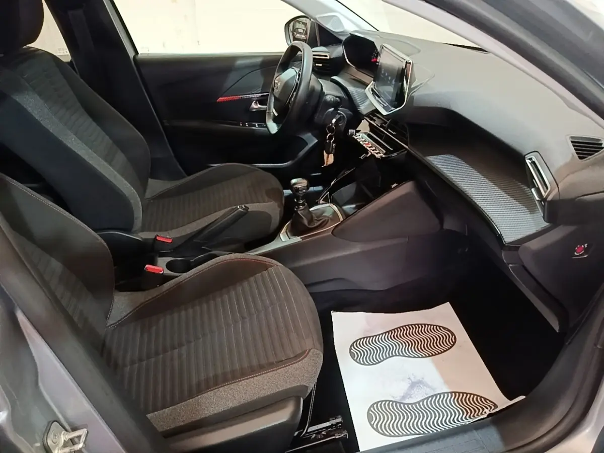 Vue intérieure côté conducteur de la Peugeot 208 gris clair 2023, volant cuir multifonctions et tableau de bord moderne.