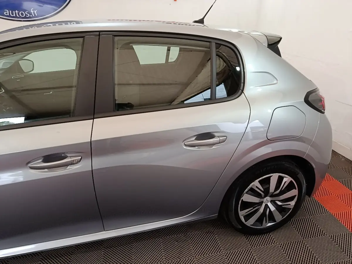 Vue latérale droite d'une Peugeot 208 gris clair, mettant en valeur la porte arrière et la jante au design moderne.