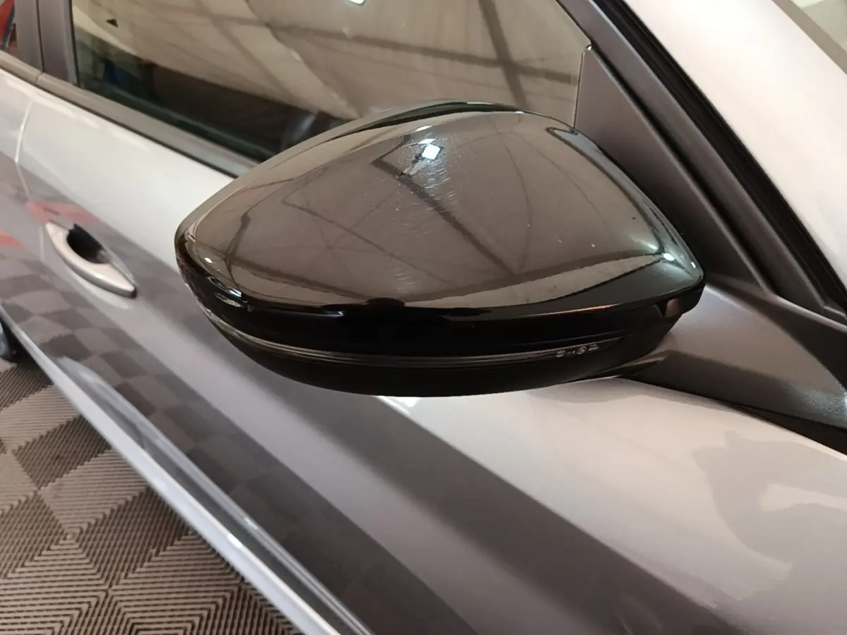 Rétroviseur noir brillant côté gauche d'une Peugeot 208 gris clair vue en gros plan depuis l'avant.