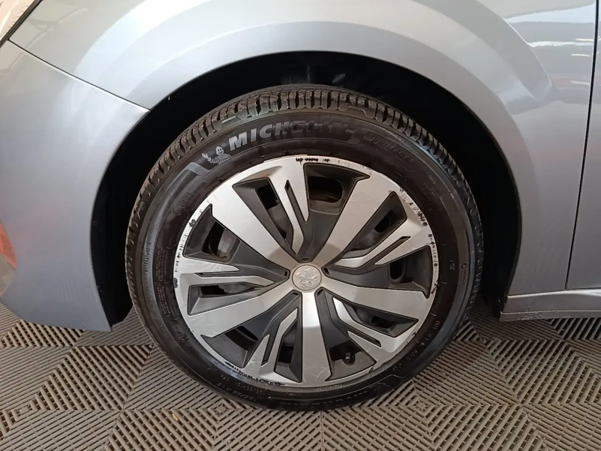 Gros plan sur la roue avant gauche gris clair d'une Peugeot 208 2023 avec jante en alliage au design moderne.