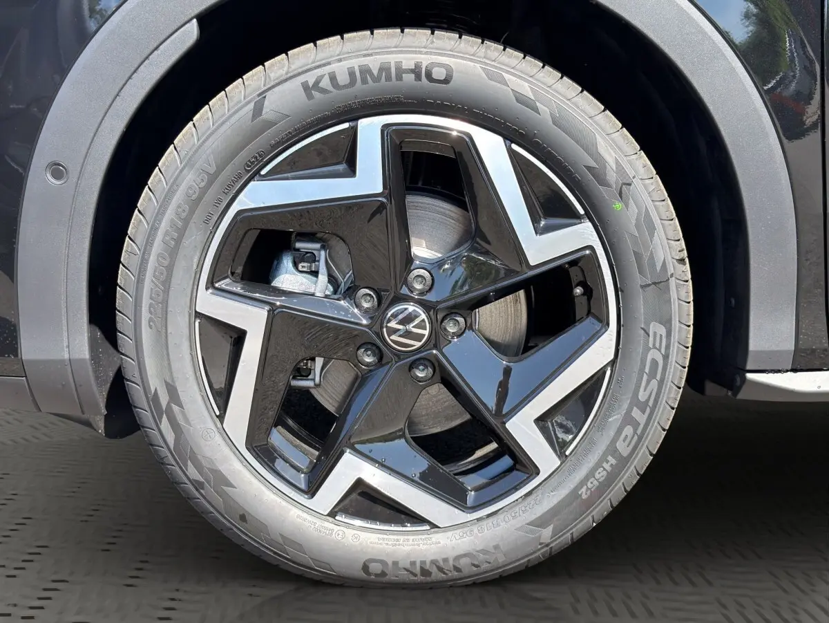 Gros plan sur la roue avant droite noire du Volkswagen T-Roc 1.5 eTSI EVO2 avec jante alliage bicolore et logo VW central.