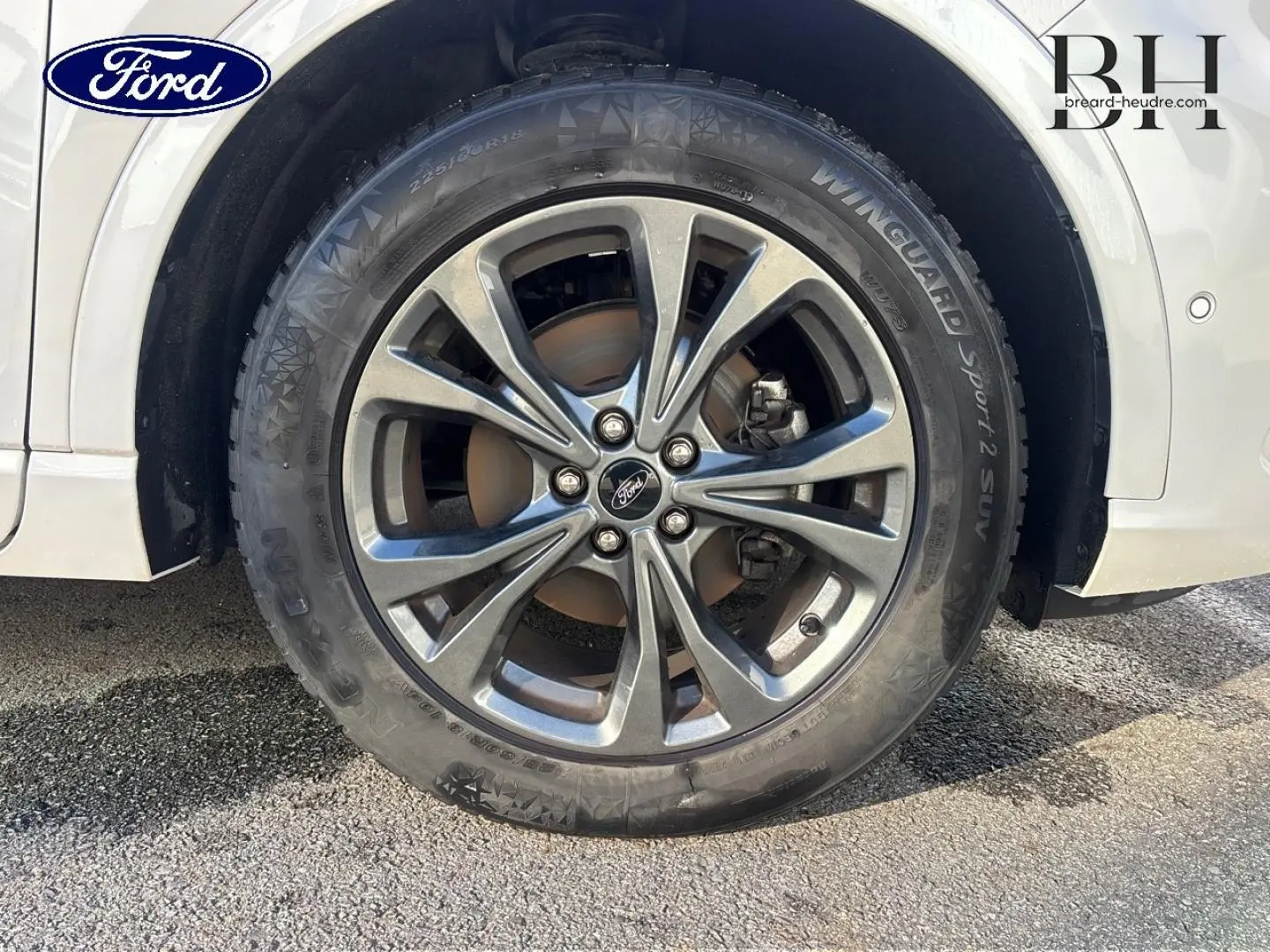 Gros plan sur la roue avant droite avec jante alliage gris du Ford Kuga blanc Premium Platinum.