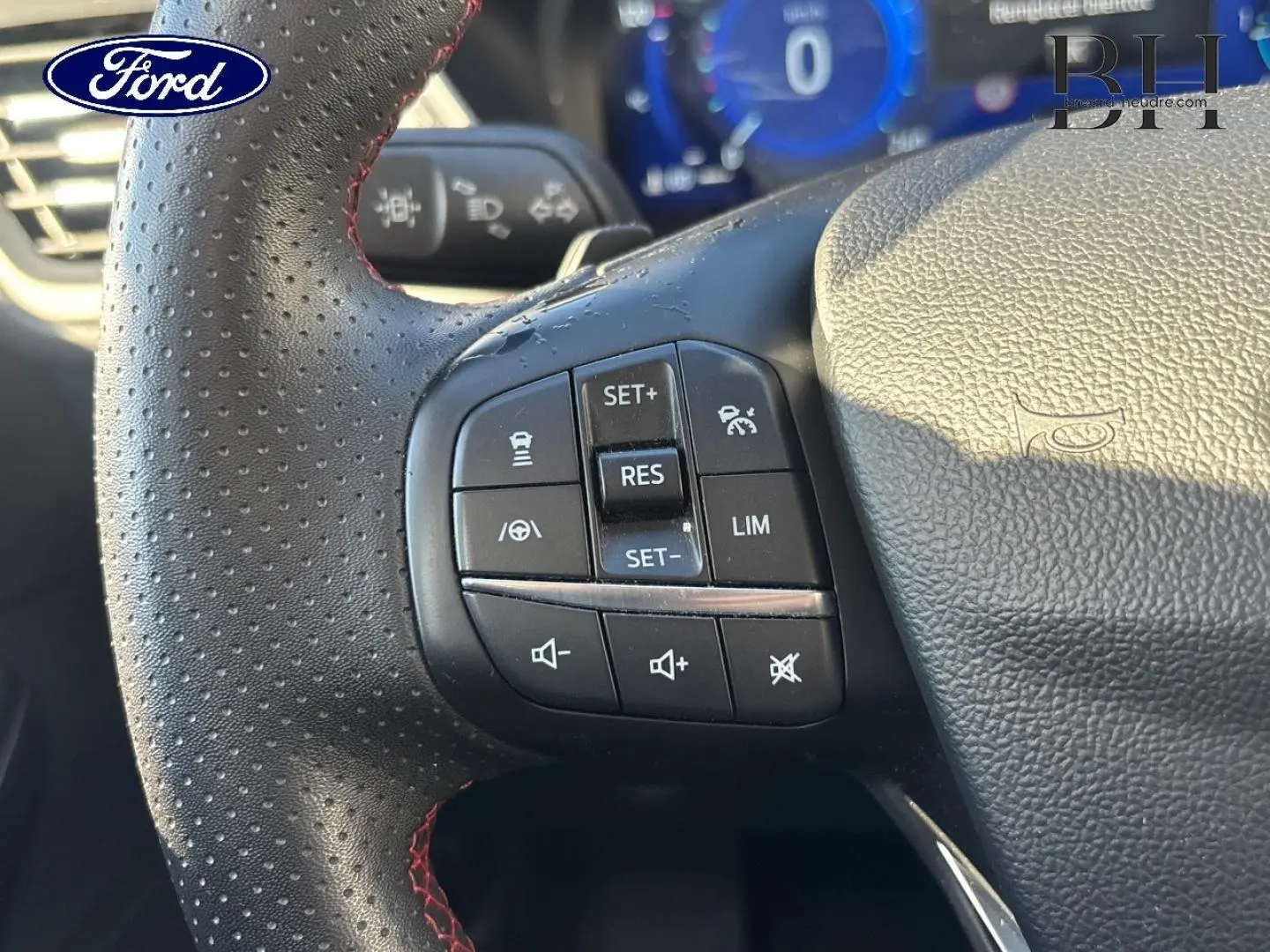 Gros plan sur le volant cuir perforé noir du Ford Kuga 2021 avec commandes multifonctions et surpiqûres rouges.