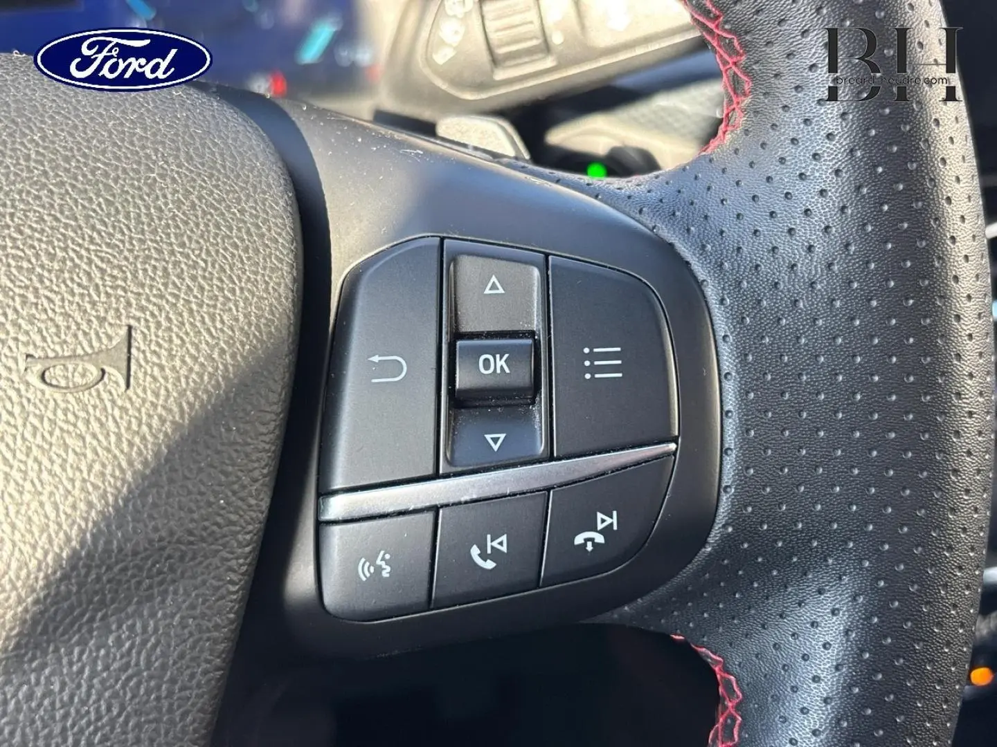 Gros plan sur les commandes multifonctions à droite du volant cuir perforé avec surpiqûres rouges du Ford Kuga blanc.