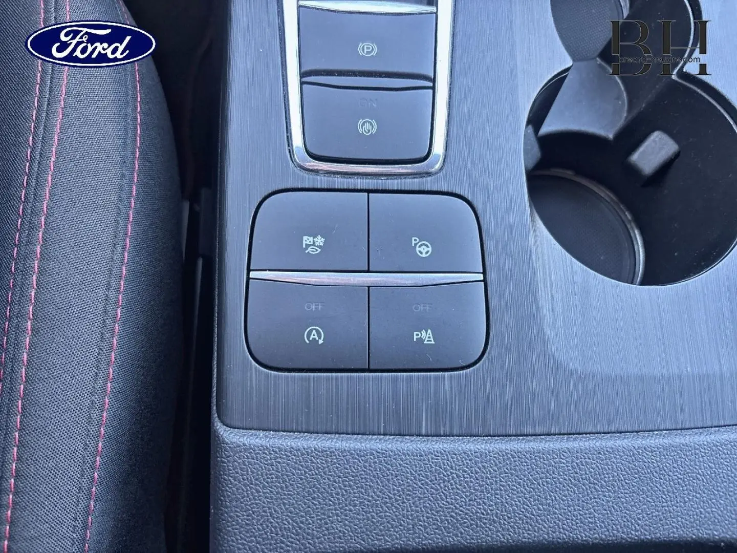 Gros plan sur la console centrale noire du Ford Kuga 2021, avec boutons de contrôle et porte-gobelets visible.