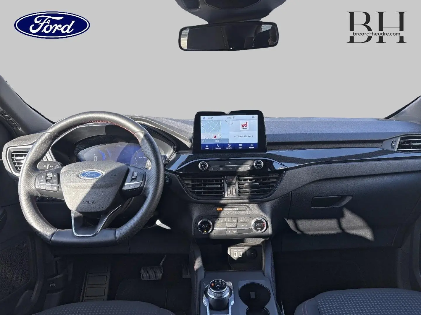 Vue frontale de l'intérieur du Ford Kuga 1.5 EcoBlue 2021, tableau de bord noir avec écran tactile et volant cuir multifonction.
