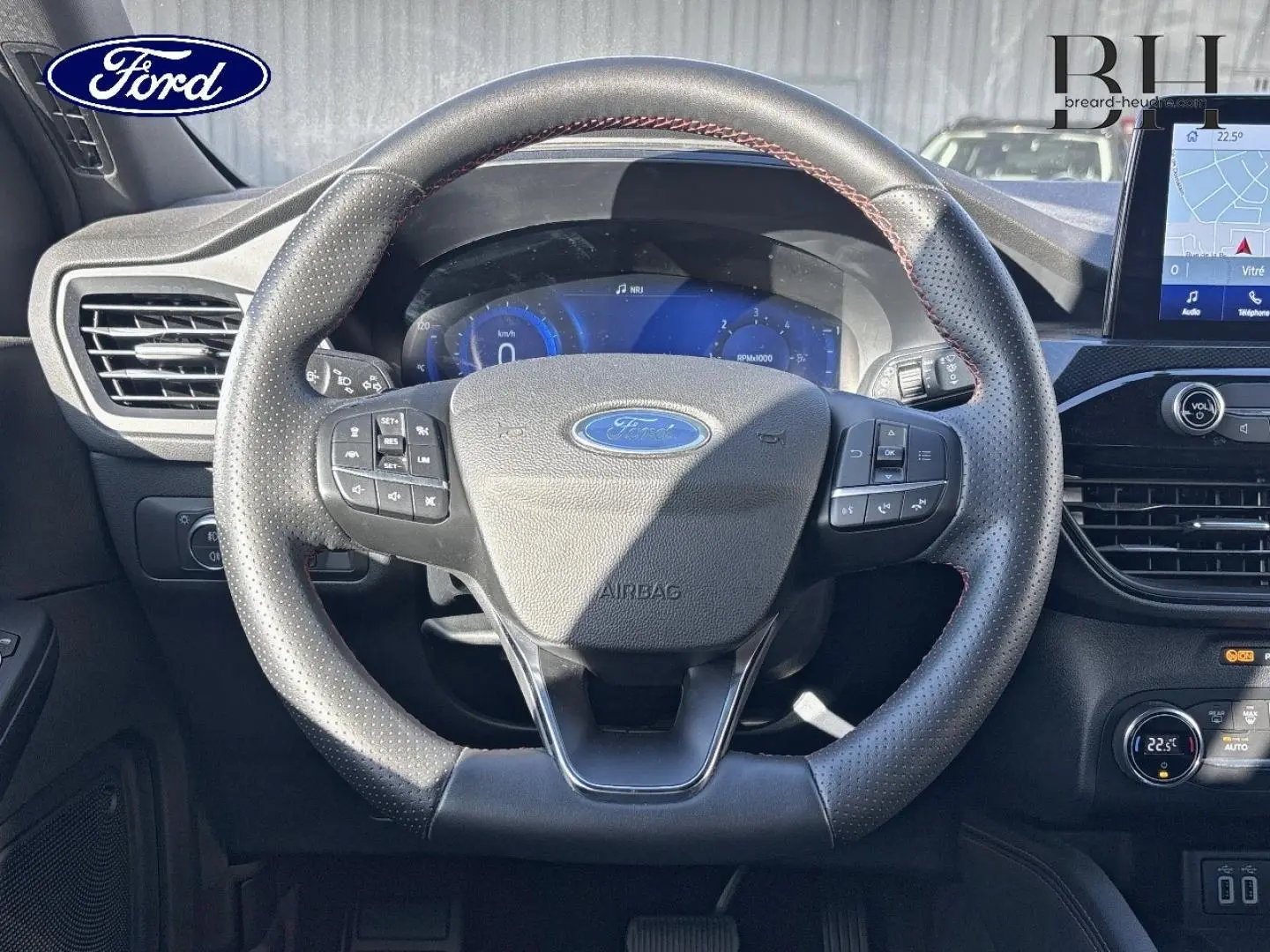 Vue intérieure frontale du volant cuir perforé du Ford Kuga 1.5 EcoBlue avec tableau de bord numérique et écran tactile.