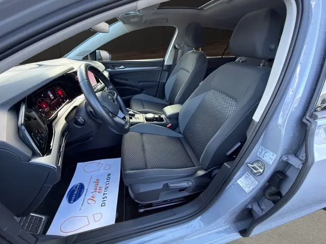 Vue intérieure côté conducteur de la Volkswagen Golf VIII gris lunaire, avec sièges tissu et tableau de bord numérique.