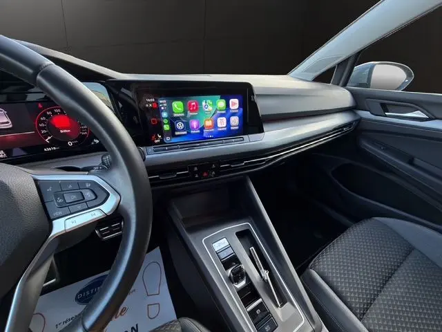 Vue intérieure côté conducteur de la Volkswagen Golf VIII gris lunaire, avec écran tactile et volant multifonction en cuir.