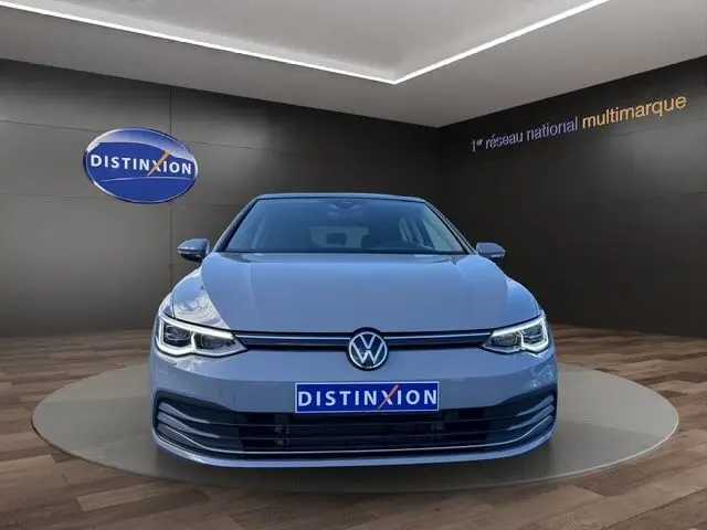 Vue avant d'une Volkswagen Golf VIII gris lunaire, avec phares LED Matrix et calandre épurée en showroom.