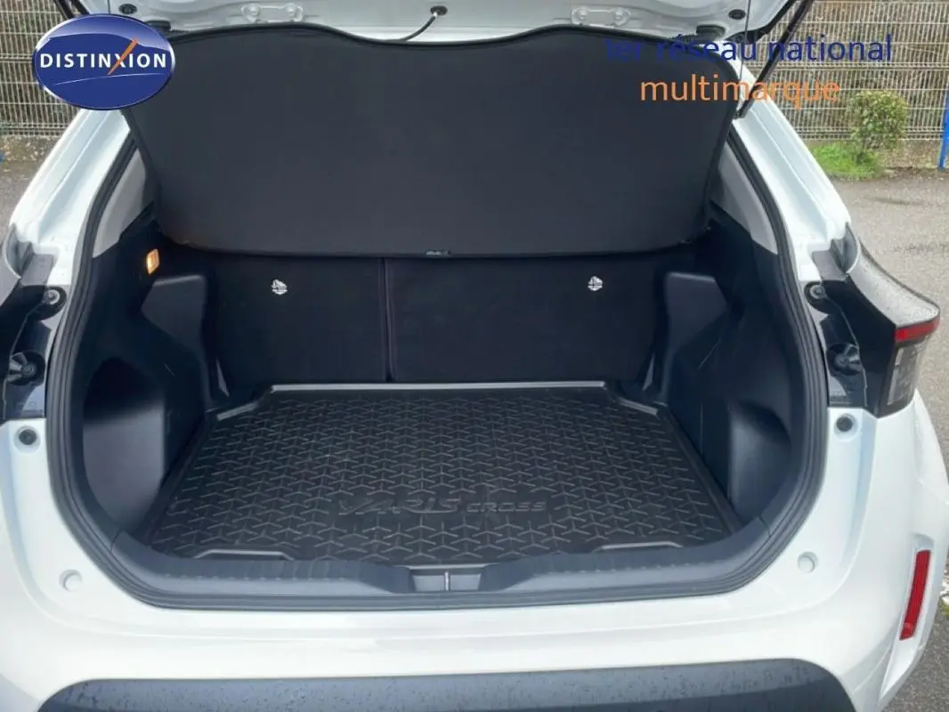 Coffre ouvert vu de l'arrière d'une Toyota Yaris Cross blanche, avec tapis de coffre noir marqué Yaris Cross.