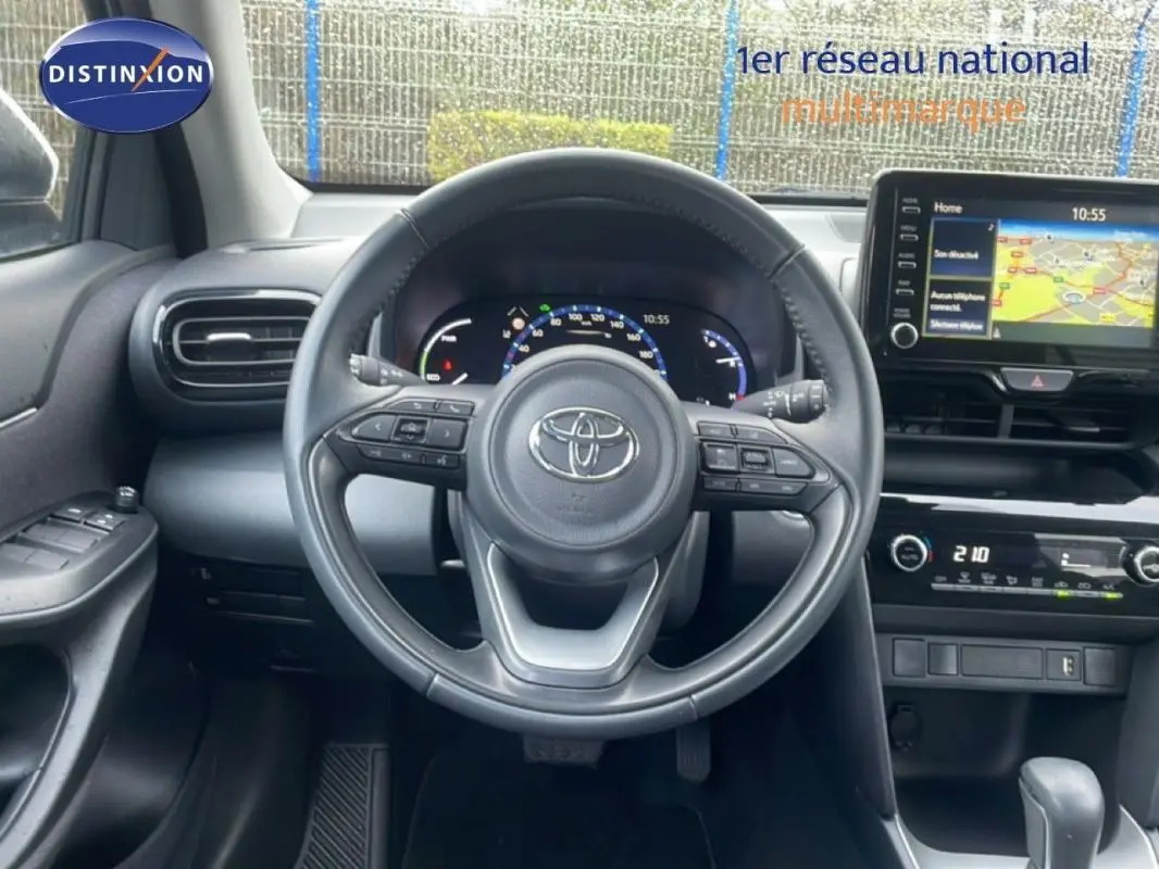 Vue intérieure centrée sur le volant cuir et le tableau de bord avec écran tactile de la Toyota Yaris Cross blanche 2024.