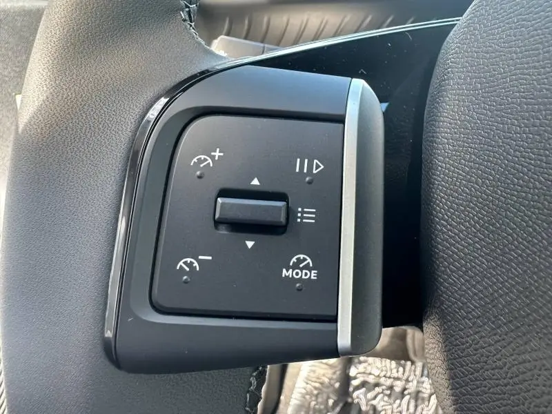 Gros plan sur les commandes noires du volant à gauche du Citroën C3 Aircross gris Mercury, boutons de régulateur et mode.