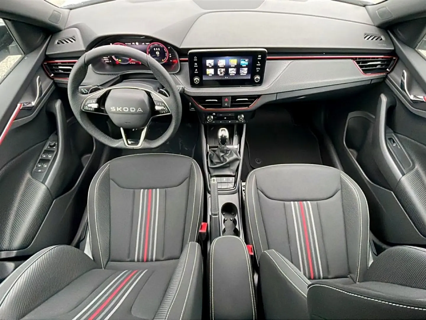 Vue intérieure avant du Skoda Kamiq 2026 Monte Carlo, sièges noirs avec bandes rouges et tableau de bord moderne avec écran tactile.