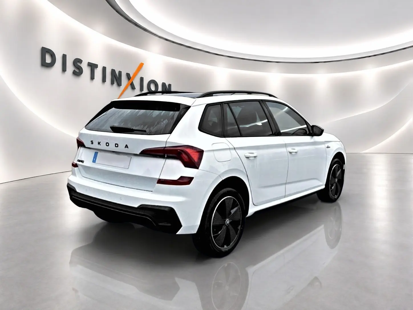 Vue 3/4 arrière droite d'un Skoda Kamiq blanc nacré avec jantes noires dans un showroom lumineux.