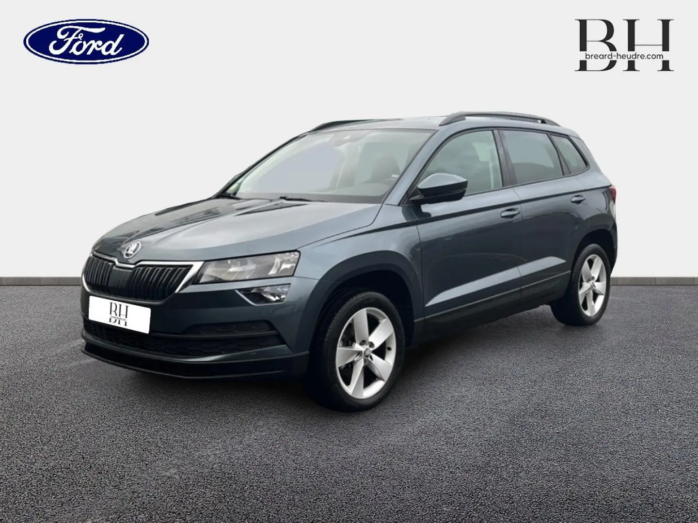 SUV Skoda Karoq gris Business vu en 3/4 avant droit, avec jantes alliage et barres de toit visibles.