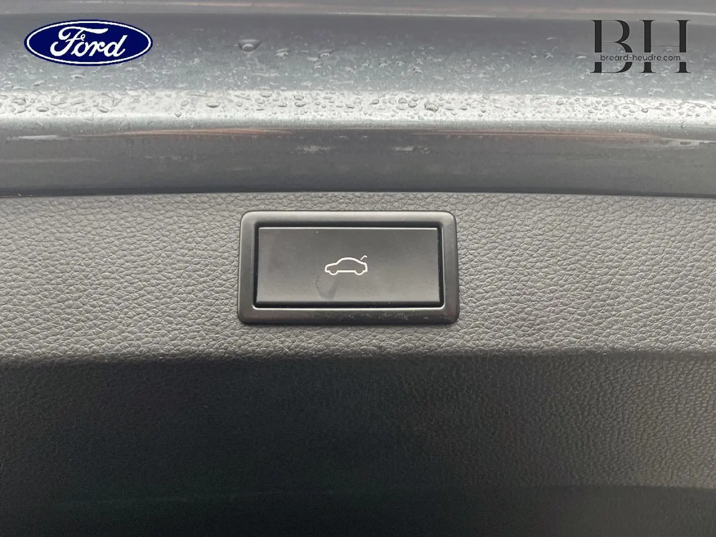 Bouton d'ouverture électrique du coffre sur la plage arrière d'un Skoda Karoq gris Business, vue rapprochée.