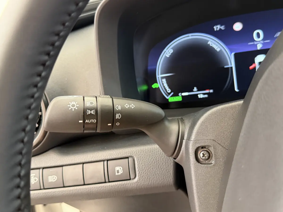 Gros plan sur la manette de phares et clignotants à gauche du volant du Toyota C-HR blanc, tableau de bord numérique visible.