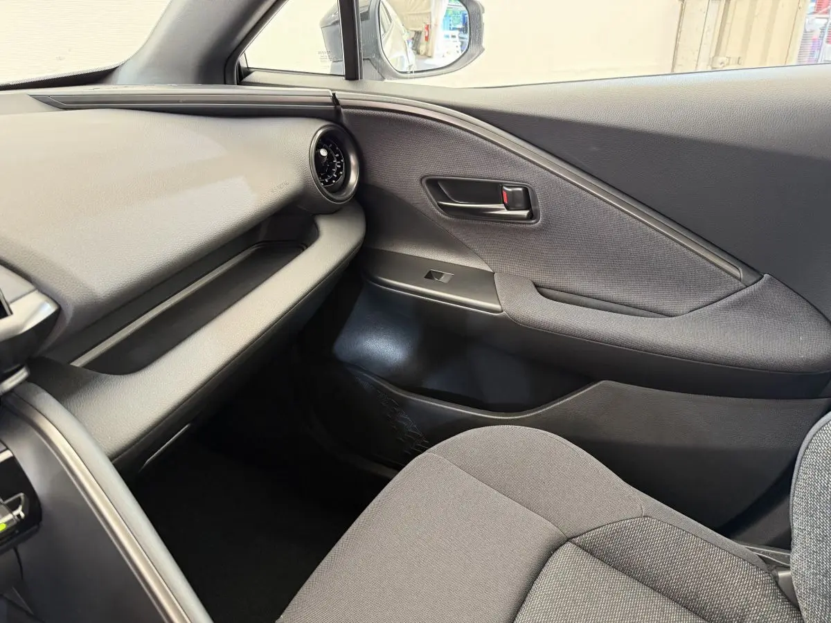Intérieur côté passager du Toyota C-HR 1.8 Hybride blanc 2024 avec tableau de bord et porte en tissu gris.
