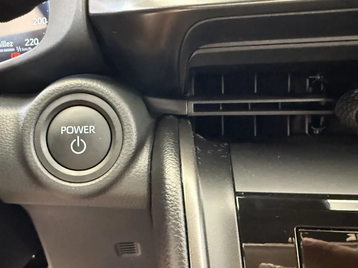 Bouton Power rond sur tableau de bord noir du Toyota C-HR 1.8 Hybride 140 Dynamic, vue intérieure rapprochée côté conducteur.