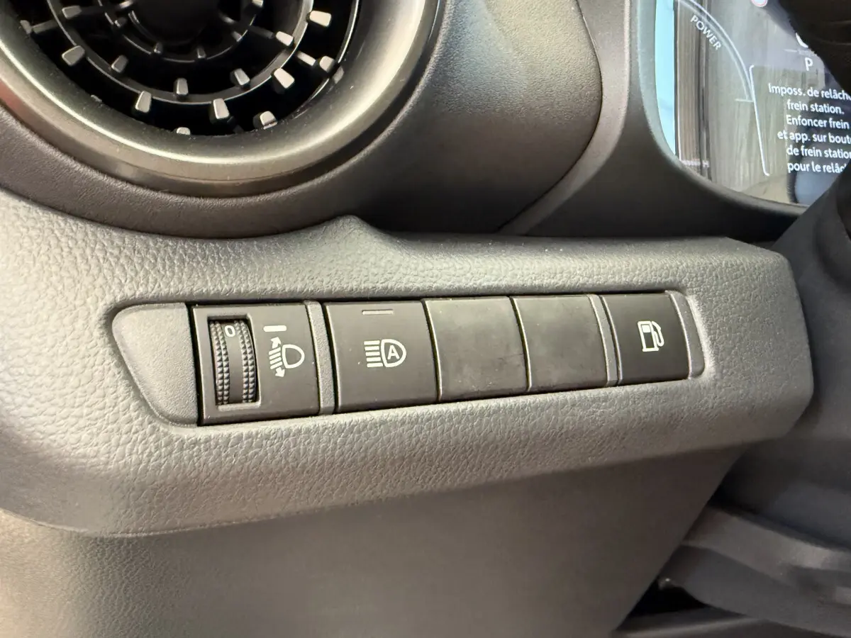 Vue rapprochée des commandes côté gauche du tableau de bord du Toyota C-HR blanc 2024, boutons d'éclairage et carburant visibles.
