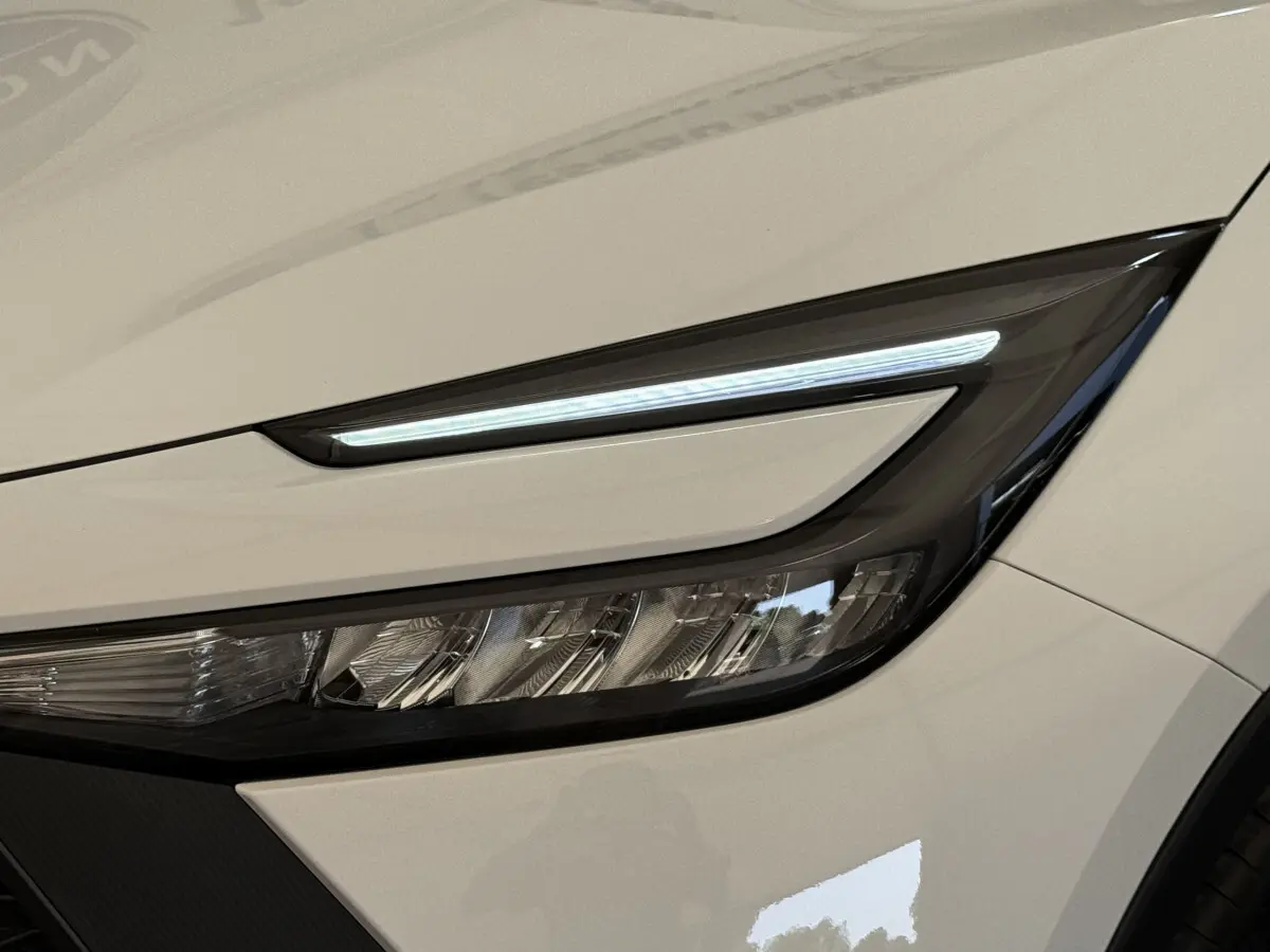 Gros plan sur le phare avant droit LED du Toyota C-HR 1.8 Hybride blanc 2024 avec ligne lumineuse fine.