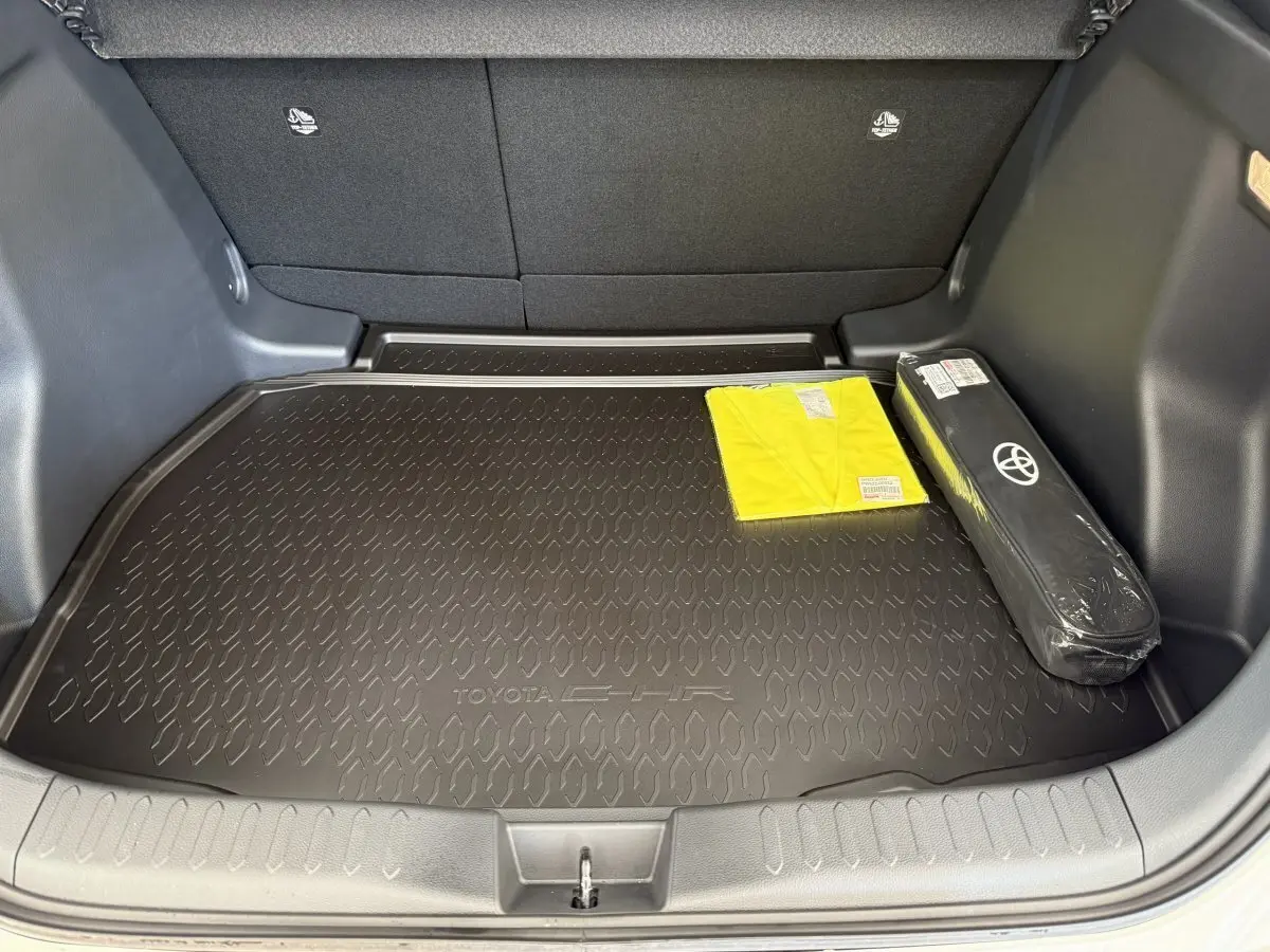 Coffre ouvert du Toyota C-HR blanc 2024 avec tapis de protection noir et accessoires de sécurité visibles.