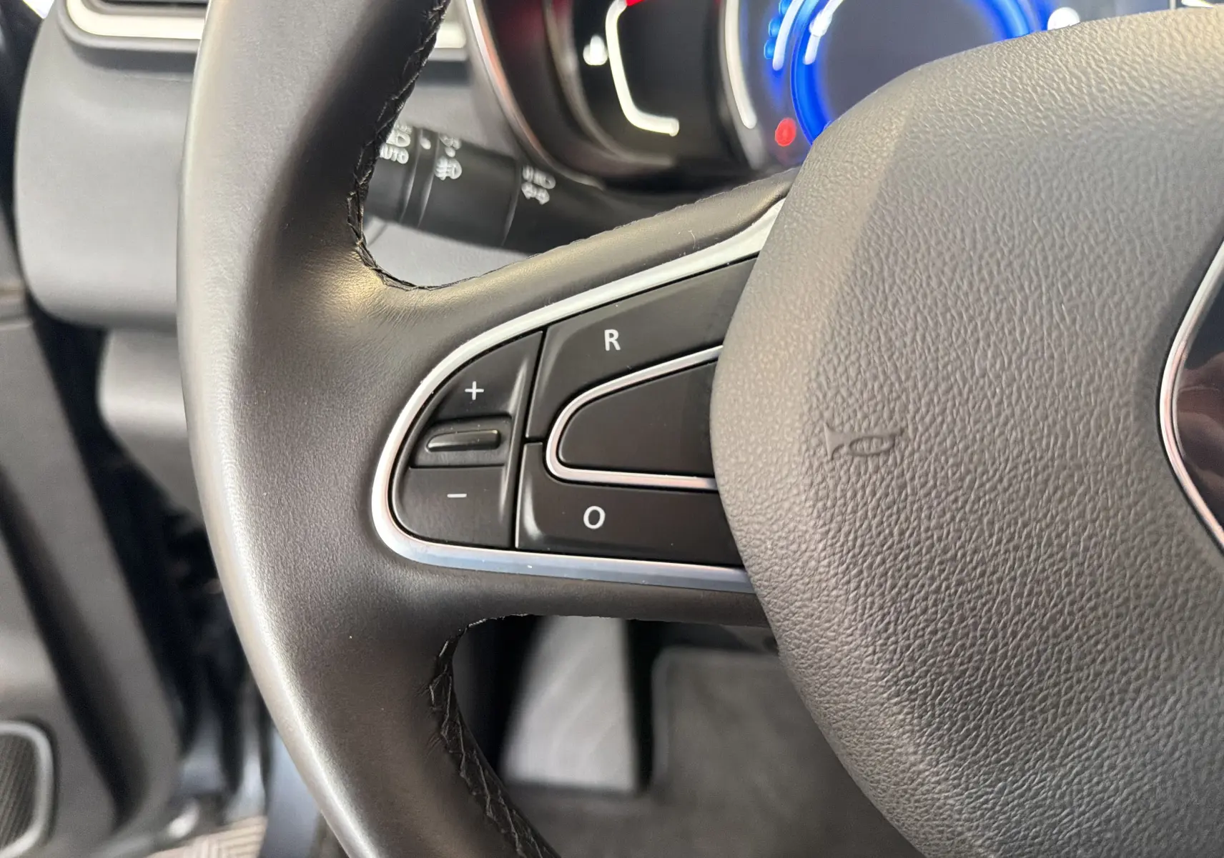 Gros plan sur les commandes au volant côté gauche du Renault Kadjar gris, avec tableau de bord numérique en arrière-plan.