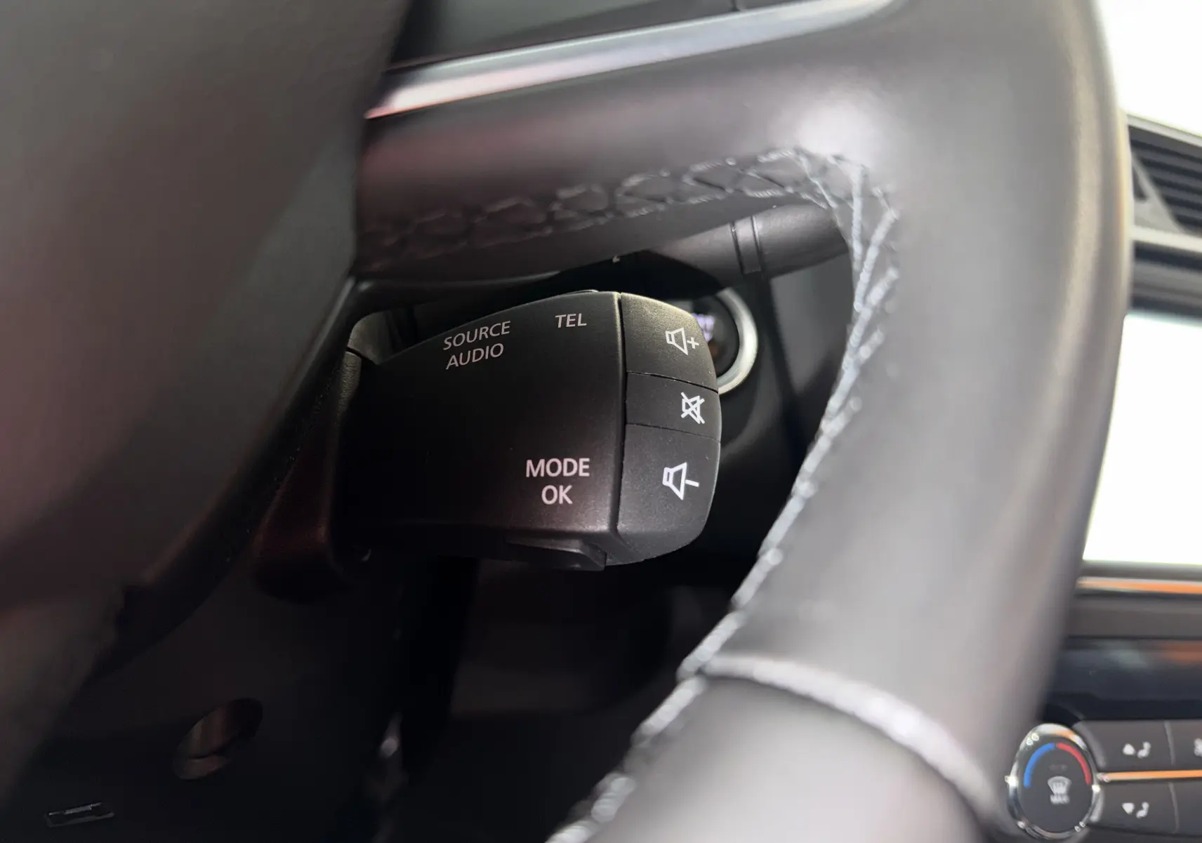 Gros plan sur la commande audio au volant noir du Renault Kadjar gris, avec boutons de volume et mode.