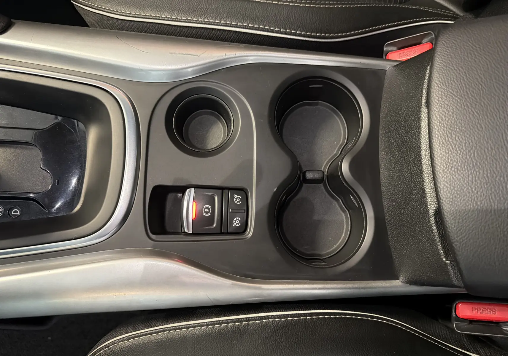 Vue plongeante sur la console centrale noire du Renault Kadjar gris, avec porte-gobelets et bouton de frein à main électronique allumé.