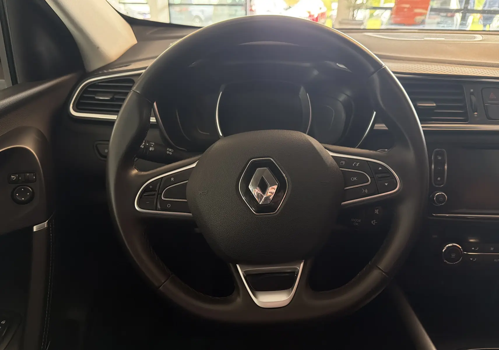 Vue rapprochée du volant noir du Renault Kadjar 2016 avec commandes intégrées et tableau de bord sombre.