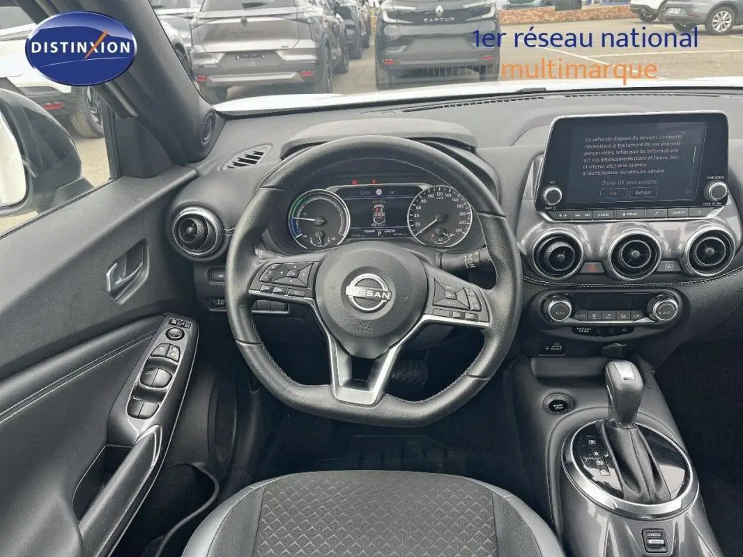 Vue intérieure avant du Nissan Juke blanc 2024, volant cuir, écran tactile et commandes au volant visibles.