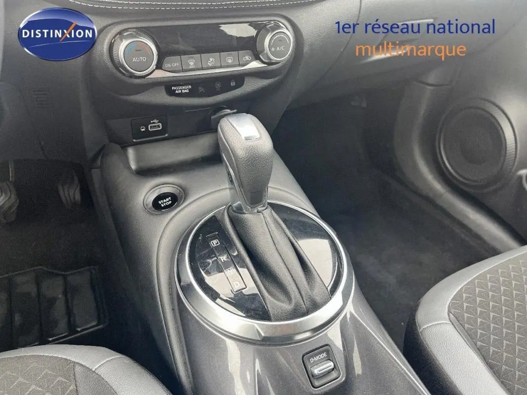 Vue rapprochée de la console centrale du Nissan Juke blanc 2024, mettant en valeur le levier de vitesse automatique et les commandes climatisation.