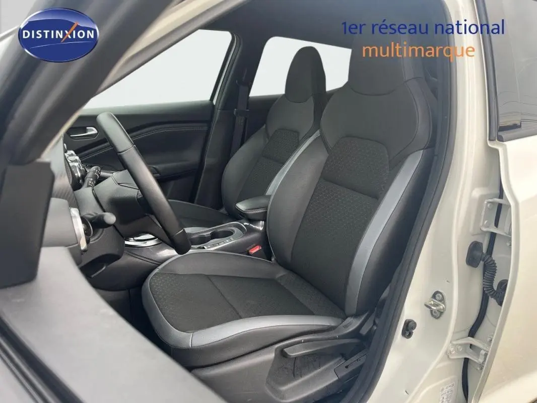 Vue intérieure côté conducteur du Nissan Juke blanc 2024, sièges noirs avec surpiqûres grises et volant cuir.