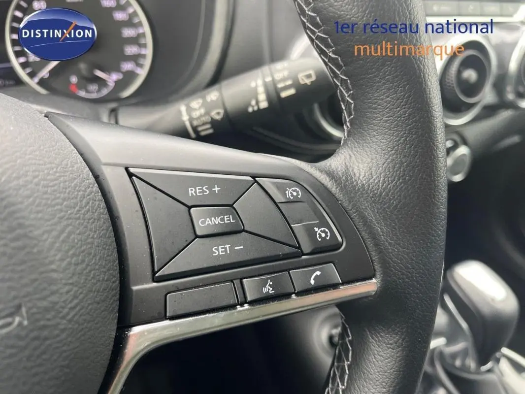 Gros plan sur les commandes du régulateur de vitesse au volant cuir noir du Nissan Juke blanc, intérieur moderne.