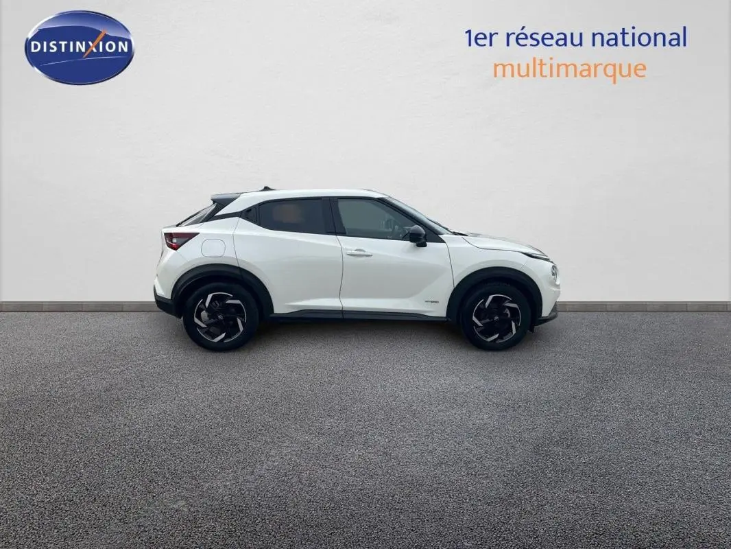Vue de profil côté gauche du Nissan Juke blanc 2024 hybride avec jantes aluminium et toit noir.