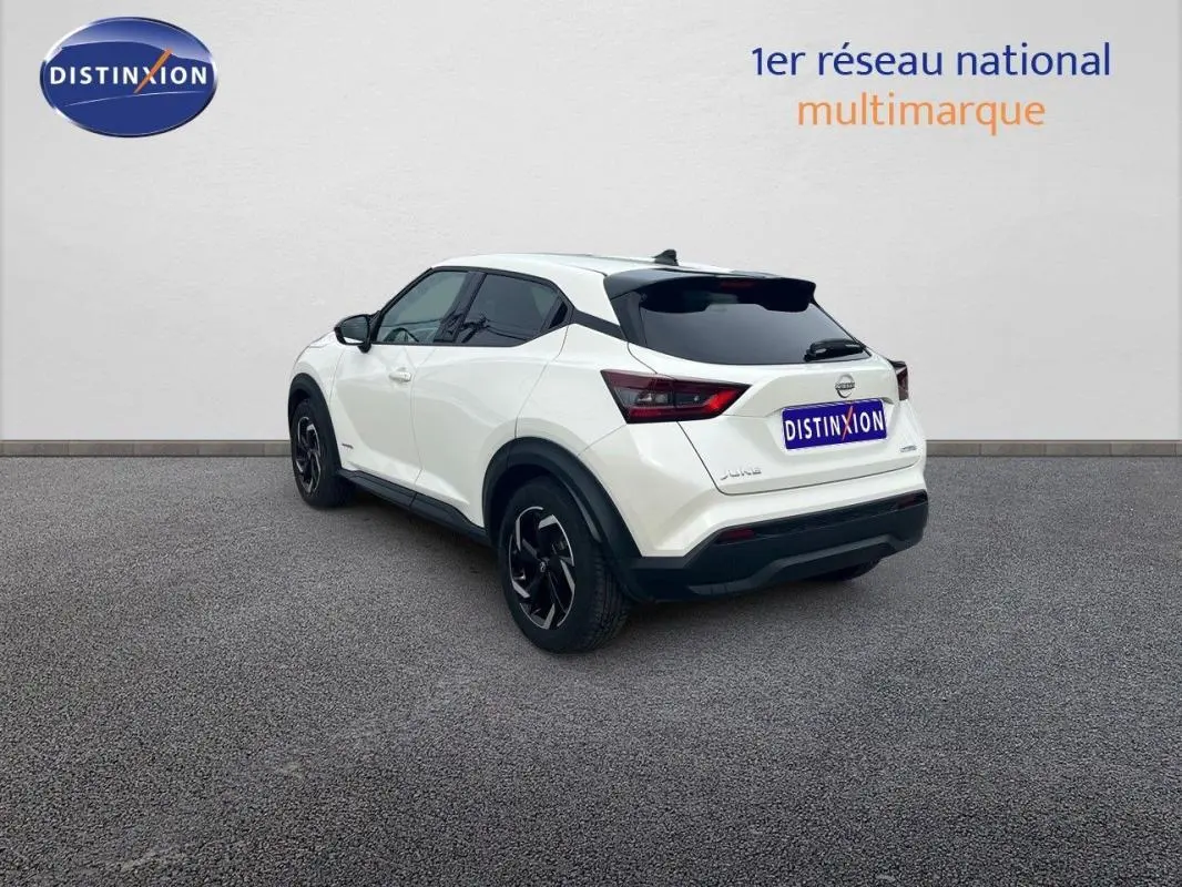 Vue 3/4 arrière droite d'un Nissan Juke blanc 2024 avec jantes aluminium et toit noir contrasté.