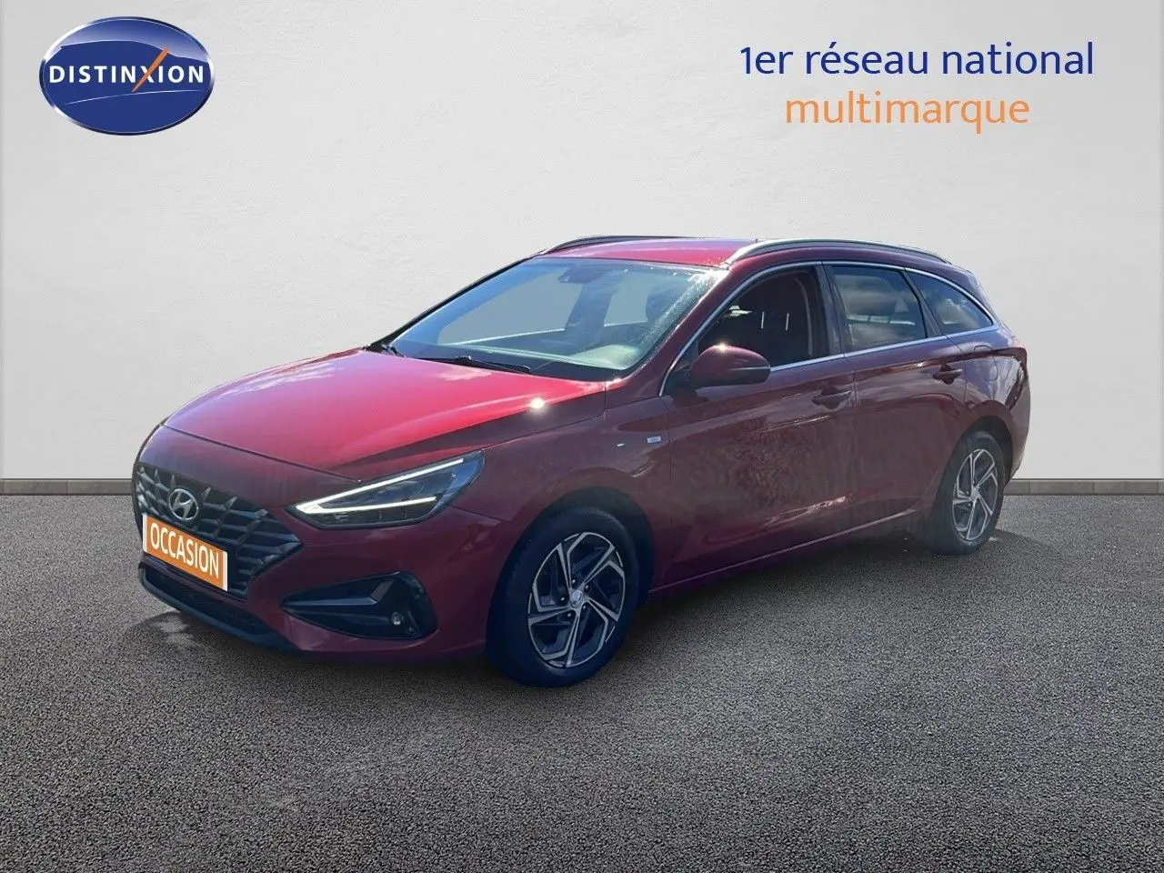 Hyundai i30 SW 2023 Sunset Red Metal vue 3/4 avant droit, avec jantes bi-ton et feux LED allumés.