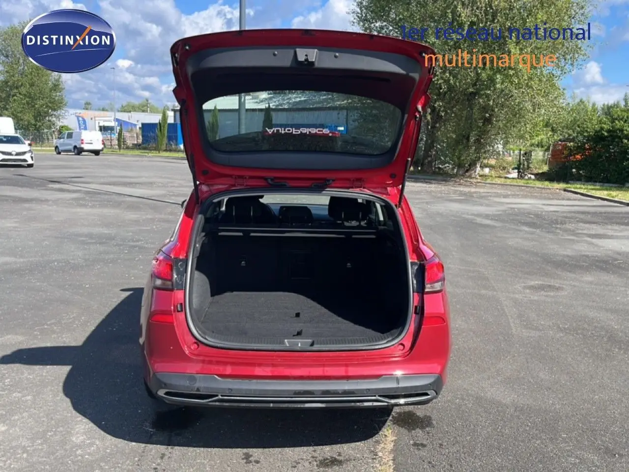 Vue arrière d’une Hyundai i30 SW 2023 en rouge Sunset Red Metal avec coffre ouvert sur un parking extérieur.