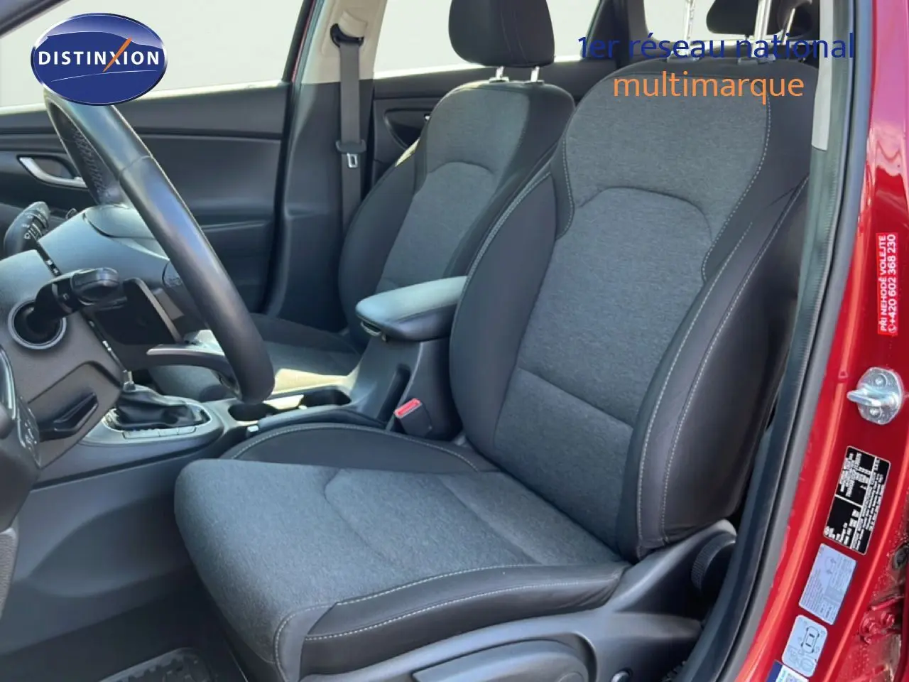 Vue intérieure côté conducteur de la Hyundai i30 SW 2023 rouge Sunset Red Metal, sièges tissu gris et cuir noir.