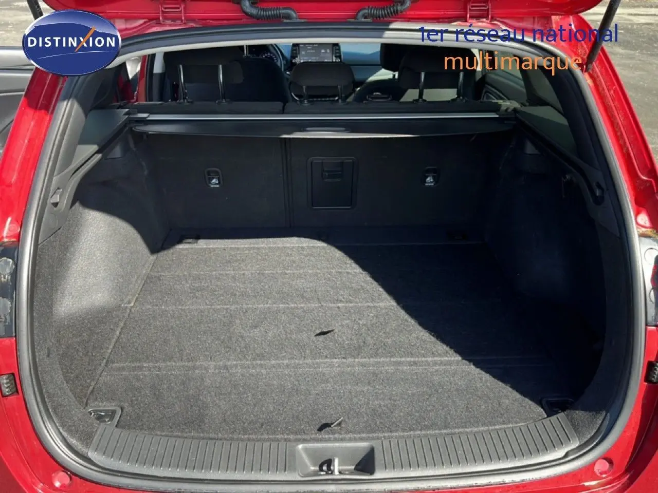 Coffre ouvert vu de l'arrière d'une Hyundai i30 SW 2023 en rouge Sunset Red Metal, intérieur noir et tapis gris.
