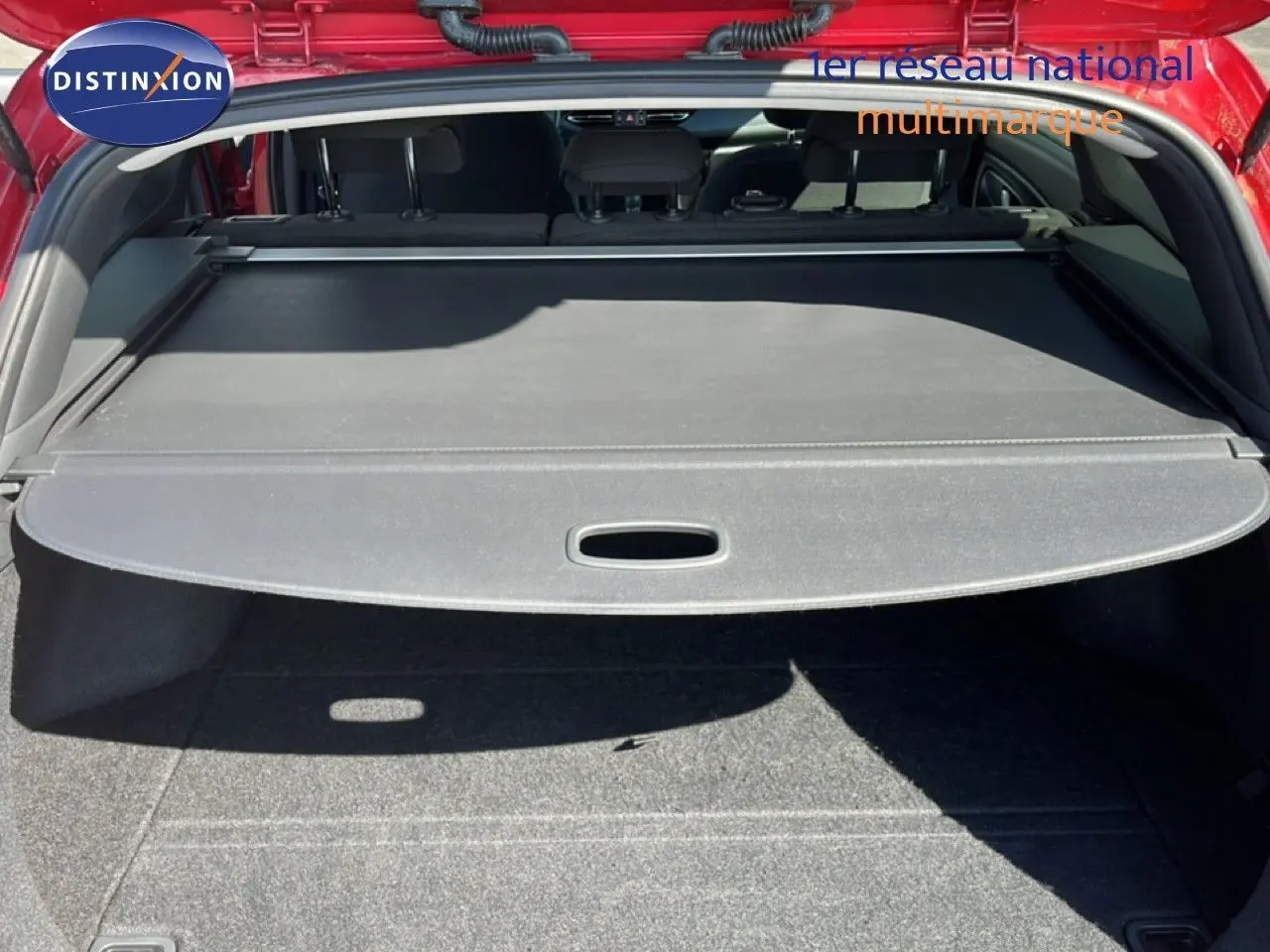Vue arrière du coffre ouvert d'une Hyundai i30 SW 2023 rouge avec cache-bagages déployé et banquette arrière visible.